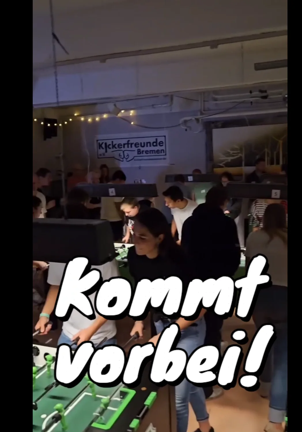 Videoausschnitt aus dem vollen Kickerraum mit dem Text „Kommt vorbei!“